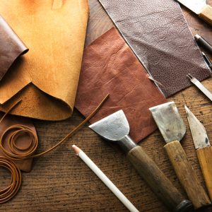 Leather craft or leather working. Leather working tools and cut out pieces of leather on leather craftman's work desk .